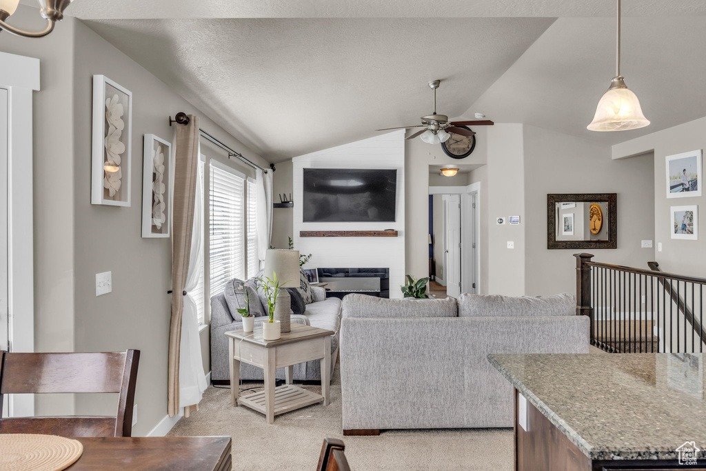 Living room with lofted ceiling, ceiling fan, a glass covered fireplace, and light colored carpet