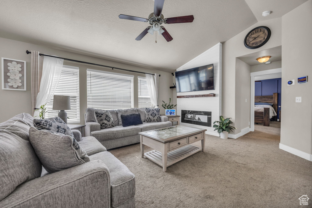 Living area with lofted ceiling, ceiling fan, carpet floors, a large fireplace, and baseboards
