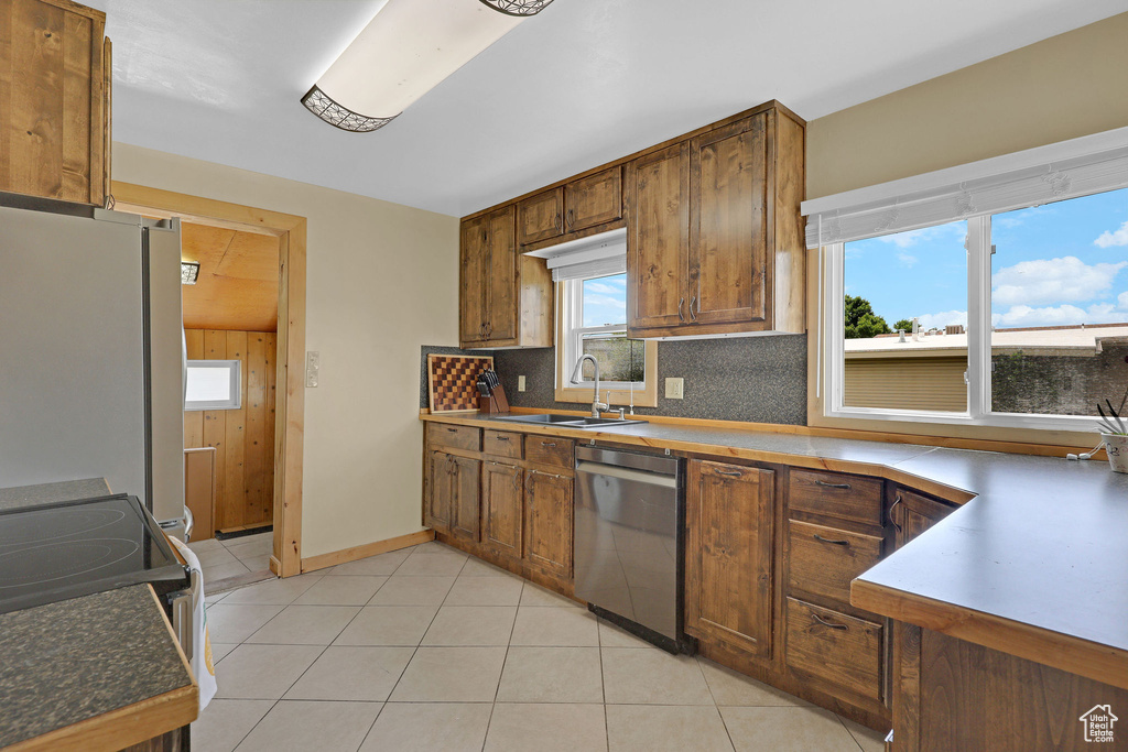 Kitchen with stainless steel appliances, a sink, backsplash, light tile patterned floors, and brown cabinets