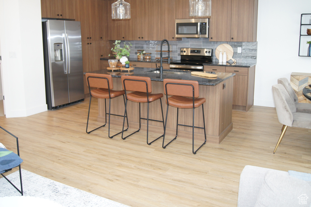 Kitchen with stainless steel appliances, a sink, brown cabinetry, tasteful backsplash, and a breakfast bar area