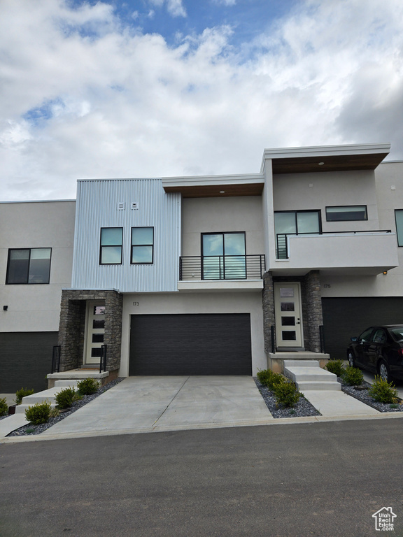 Modern home featuring stone siding, a balcony, stucco siding, and an attached garage