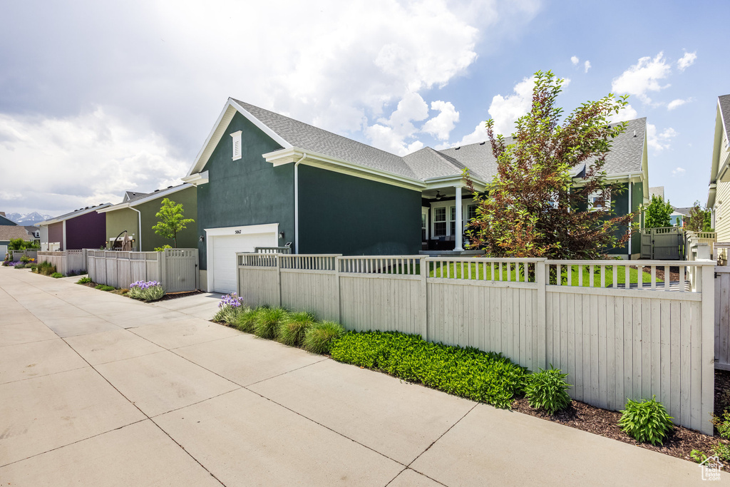 View of side of home featuring a fenced front yard, an attached garage, stucco siding, driveway, and a shingled roof