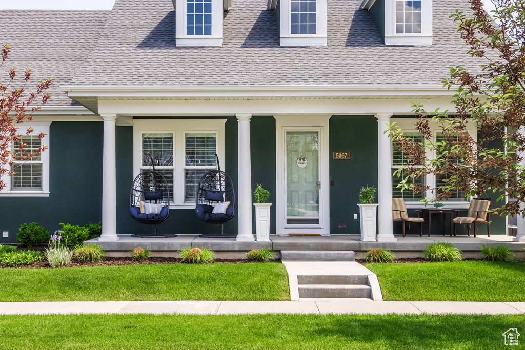Entrance to property with a porch, a shingled roof, and stucco siding
