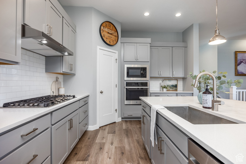 Kitchen with appliances with stainless steel finishes, extractor fan, gray cabinetry, a sink, and backsplash