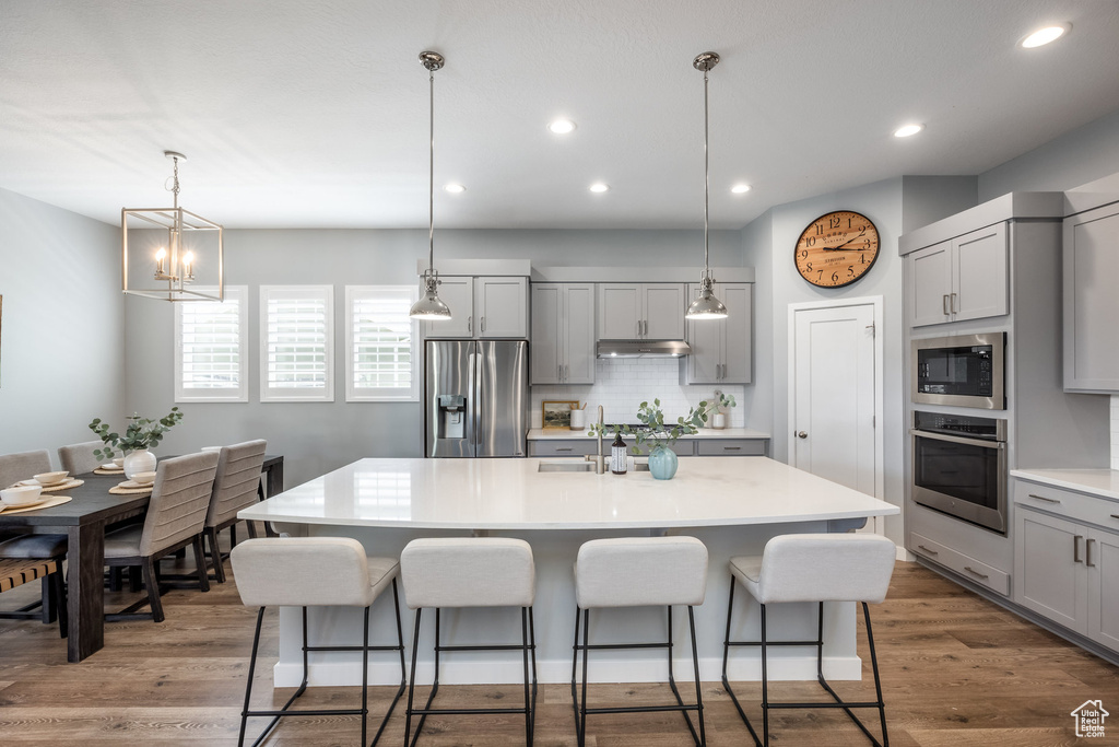 Kitchen featuring stainless steel appliances, gray cabinetry, under cabinet range hood, a breakfast bar, and recessed lighting