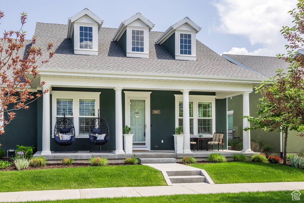 View of front of property with covered porch, a shingled roof, a front lawn, and stucco siding