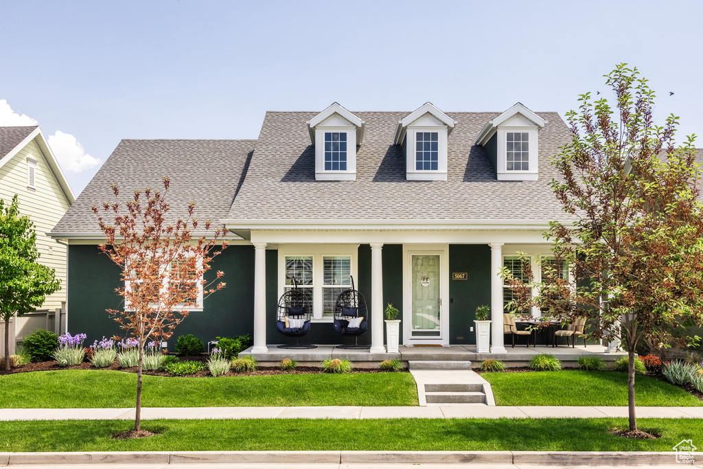 Cape cod house featuring covered porch, roof with shingles, a front yard, and stucco siding