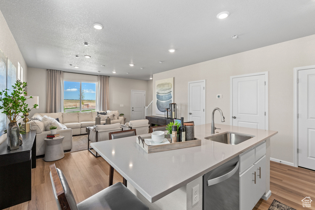Kitchen with a sink, stainless steel dishwasher, white cabinetry, a center island with sink, and light wood-type flooring