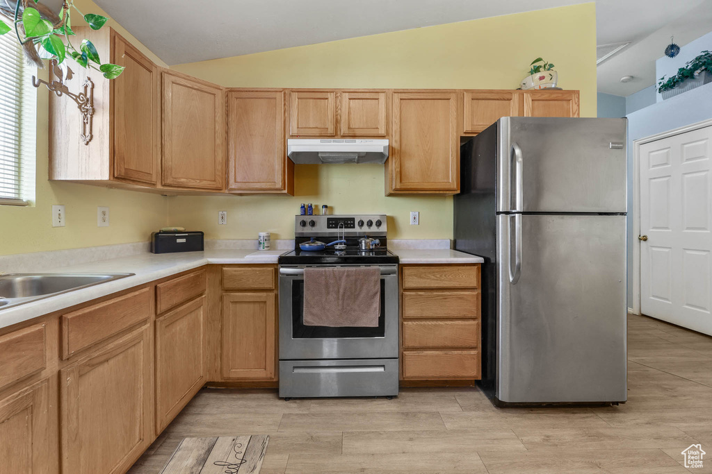 Kitchen with appliances with stainless steel finishes, under cabinet range hood, light countertops, vaulted ceiling, and light wood finished floors