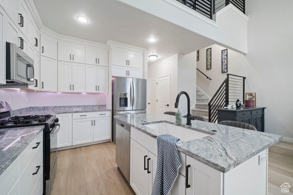Kitchen with stainless steel appliances, a sink, light wood finished floors, white cabinets, and an island with sink