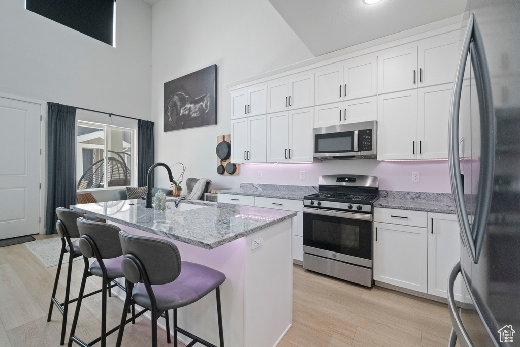 Kitchen featuring appliances with stainless steel finishes, high vaulted ceiling, a sink, light stone countertops, and a kitchen bar