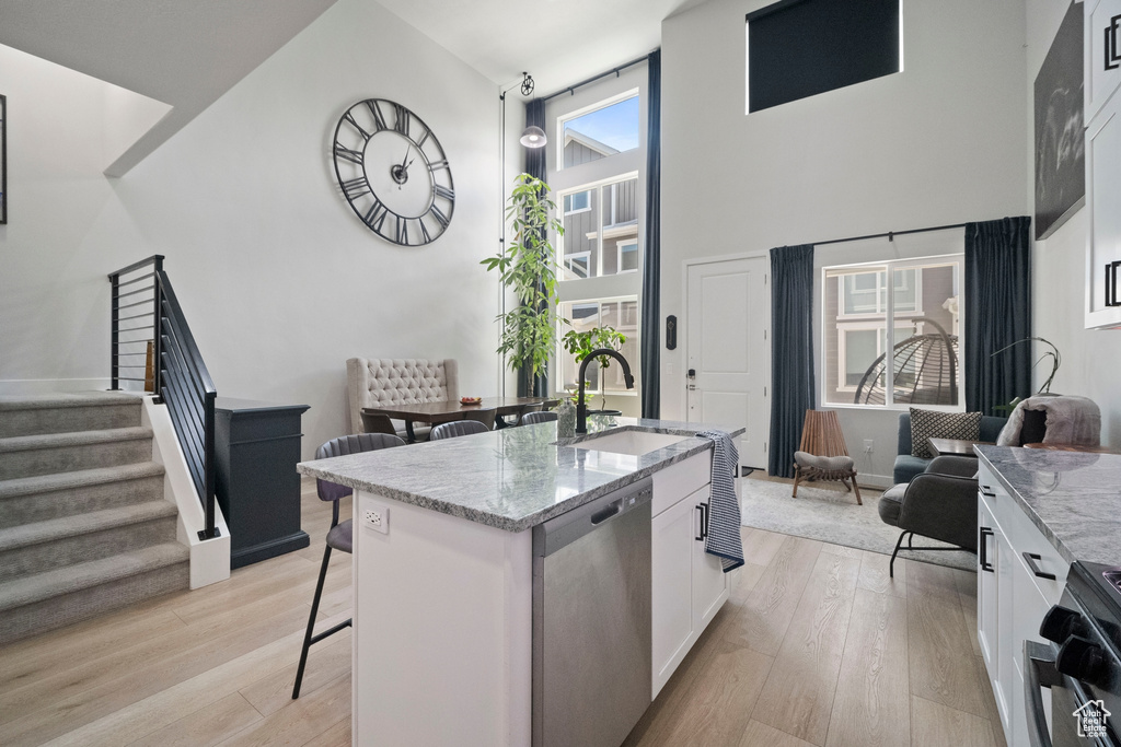 Kitchen with appliances with stainless steel finishes, a sink, a kitchen bar, white cabinets, and light stone countertops