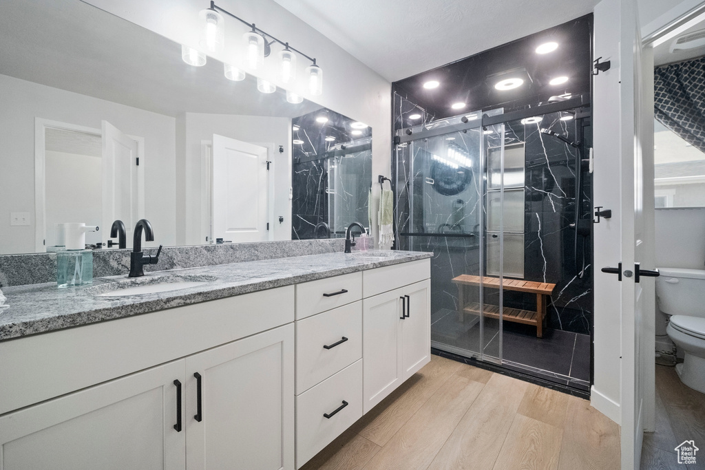 Full bathroom featuring toilet, double vanity, wood finished floors, and a marble finish shower