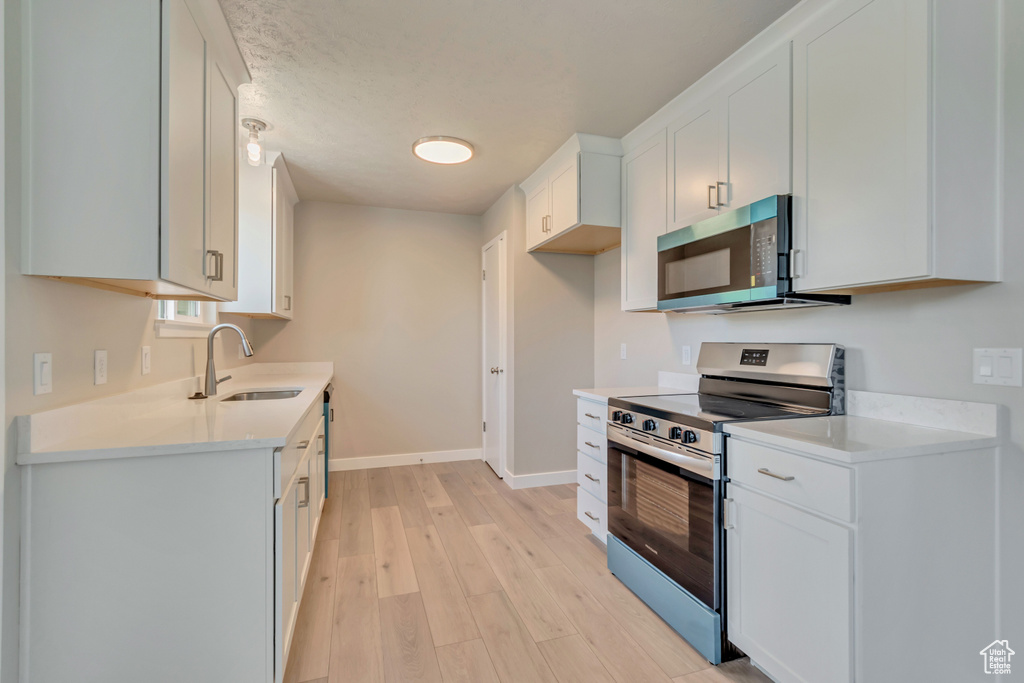 Kitchen with appliances with stainless steel finishes, a sink, baseboards, light wood-type flooring, and light countertops