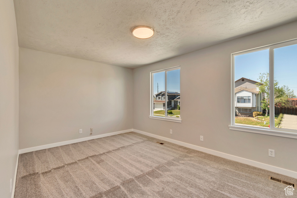 Unfurnished room featuring a textured ceiling, light colored carpet, and baseboards