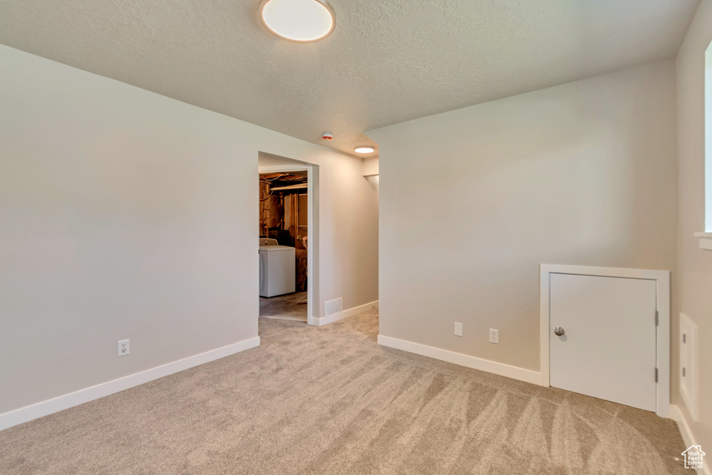 Spare room with a textured ceiling, carpet floors, washer / clothes dryer, and baseboards