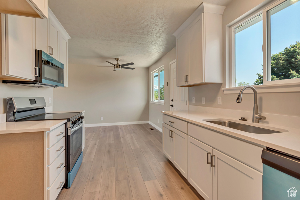 Kitchen with stainless steel electric range oven, a sink, dishwasher, light wood-style floors, and light countertops