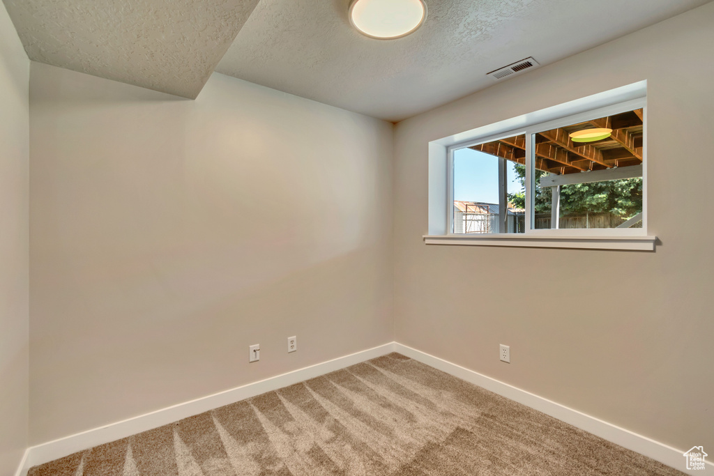 Carpeted empty room with a textured ceiling and baseboards