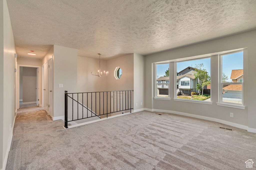 Carpeted empty room featuring a textured ceiling, a chandelier, and baseboards