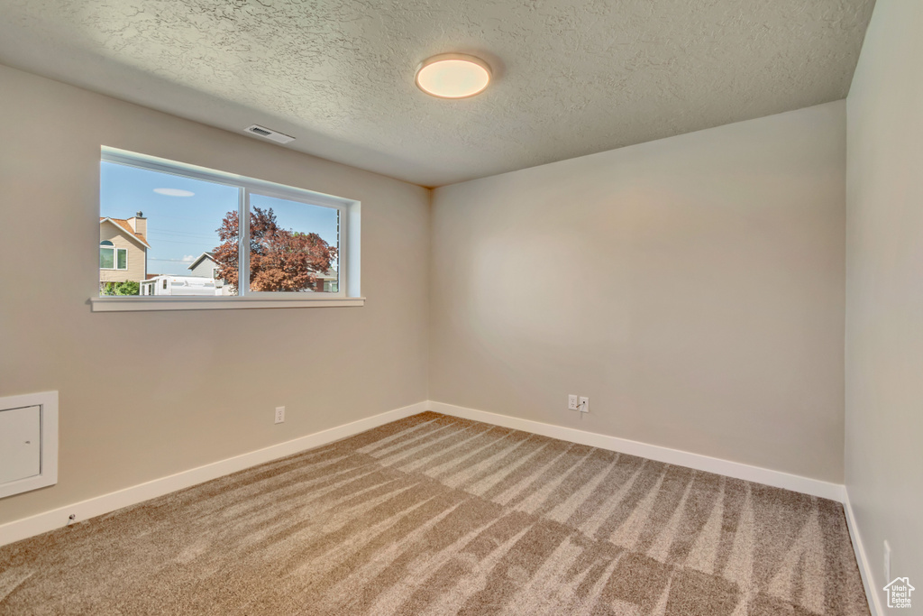 Carpeted spare room featuring a textured ceiling and baseboards