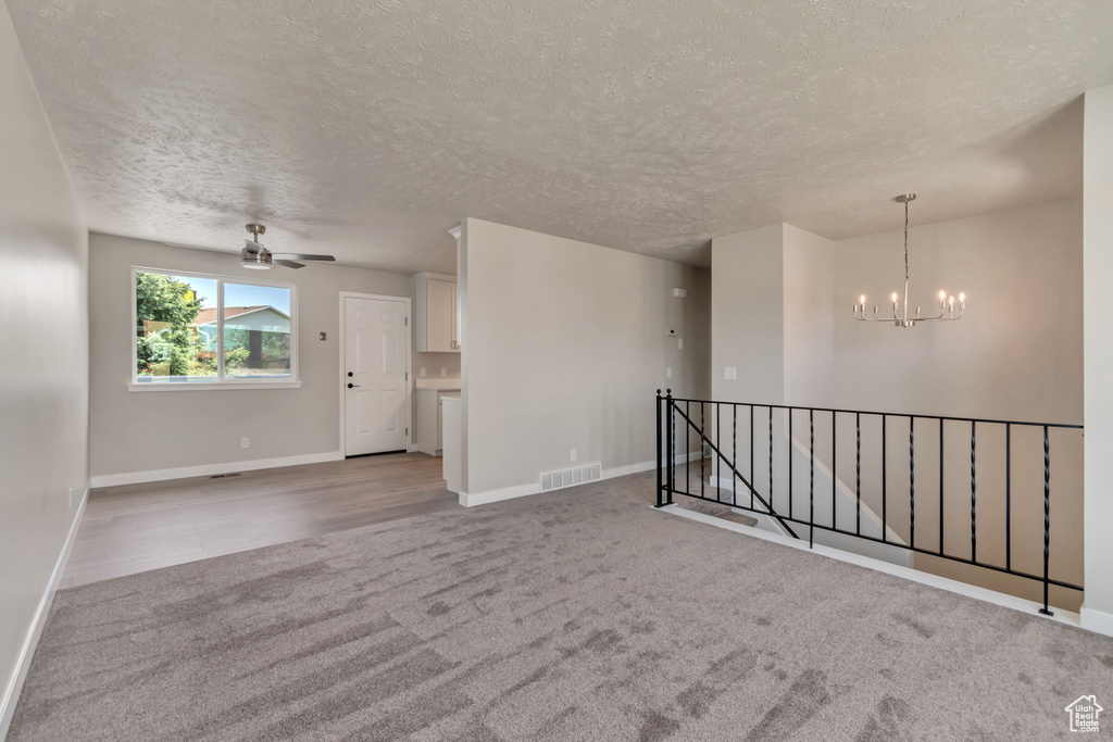 Unfurnished room featuring a chandelier, carpet, baseboards, a ceiling fan, and a textured ceiling