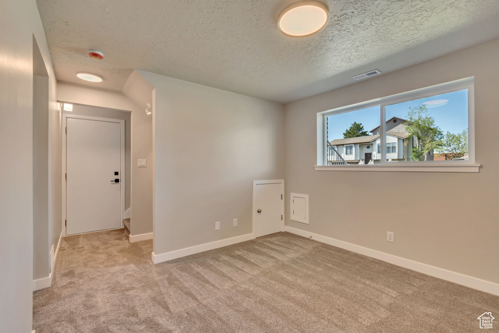 Empty room with a textured ceiling, carpet flooring, baseboards, and a smoke detector