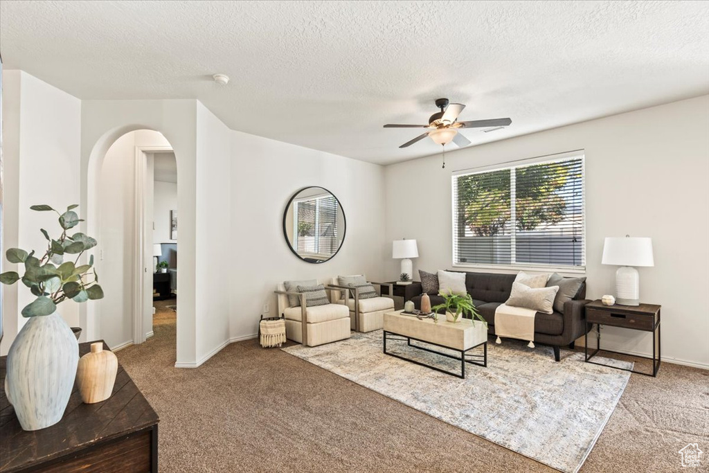 Carpeted living room featuring arched walkways, ceiling fan, a textured ceiling, and baseboards
