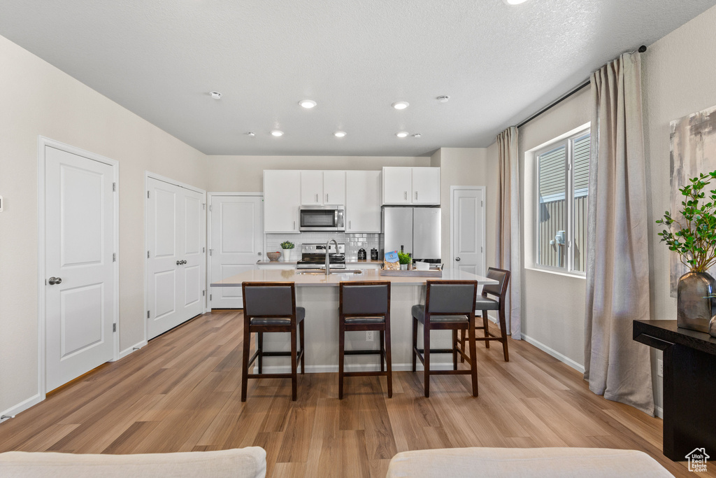 Kitchen featuring appliances with stainless steel finishes, a sink, light wood finished floors, a breakfast bar, and white cabinets