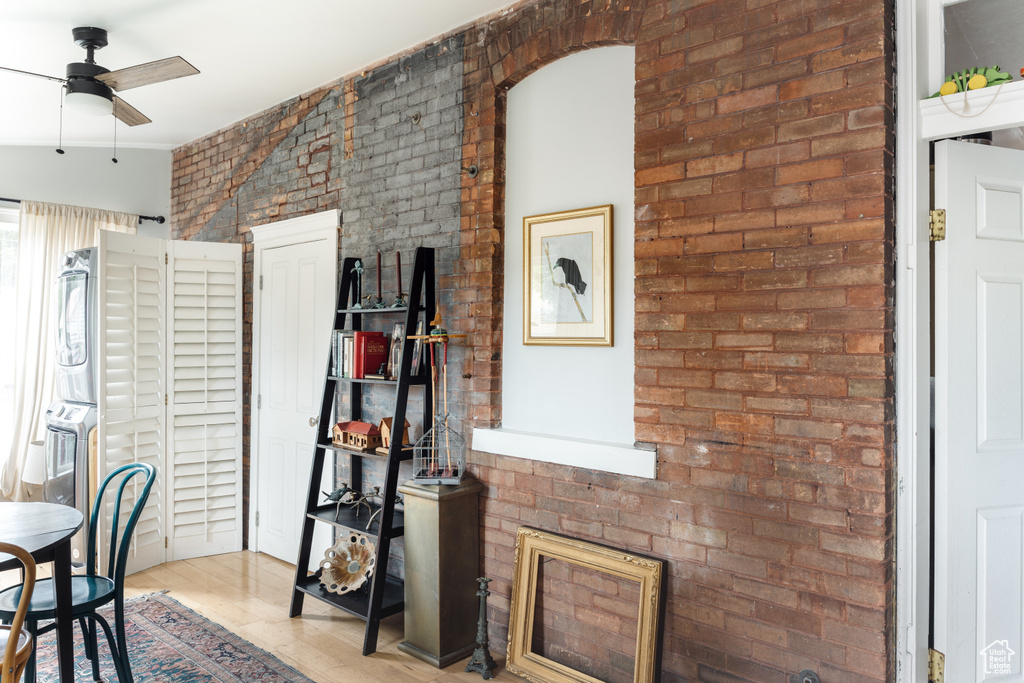 Dining space with ceiling fan, wood finished floors, and brick wall