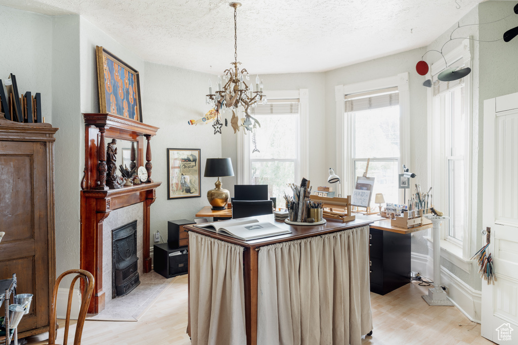Home office with light wood-style flooring, a chandelier, a tile fireplace, and a textured ceiling