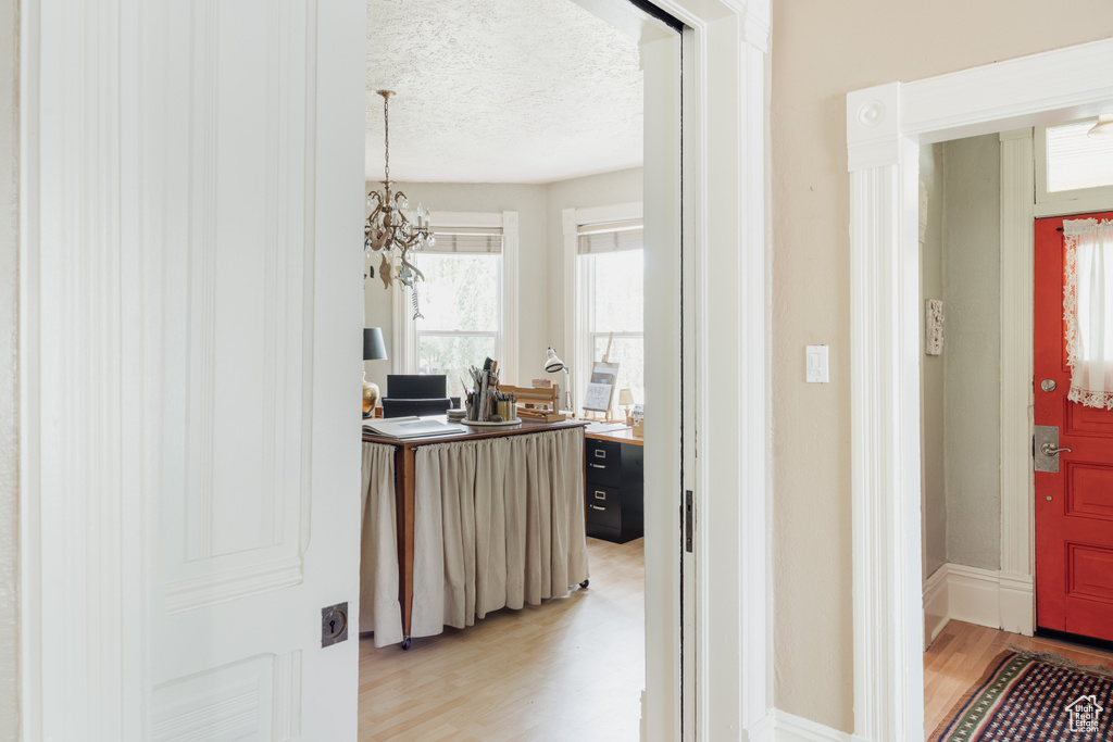 Hall featuring light wood finished floors, a textured ceiling, and a chandelier