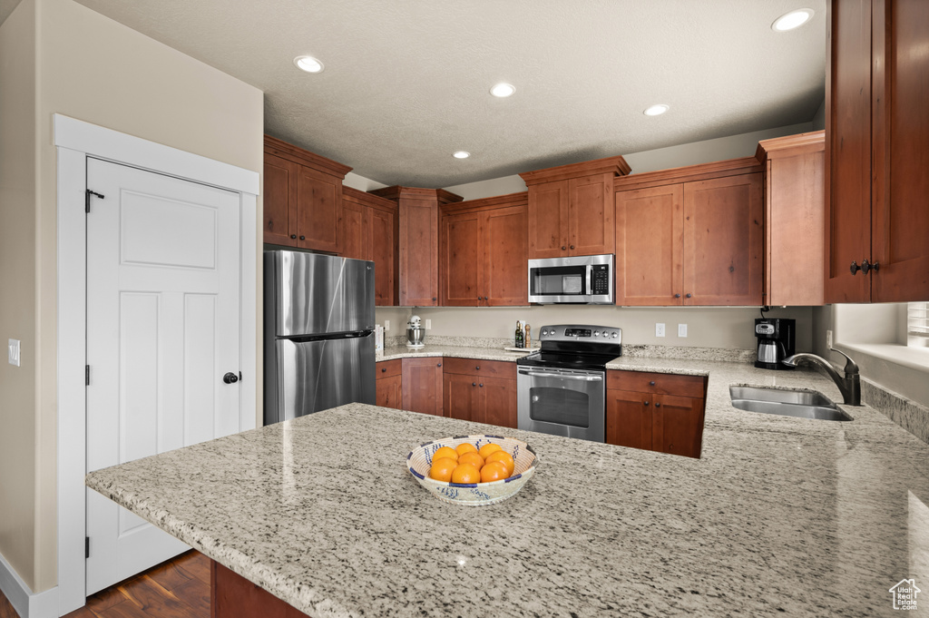 Kitchen featuring appliances with stainless steel finishes, a sink, a peninsula, recessed lighting, and light stone countertops