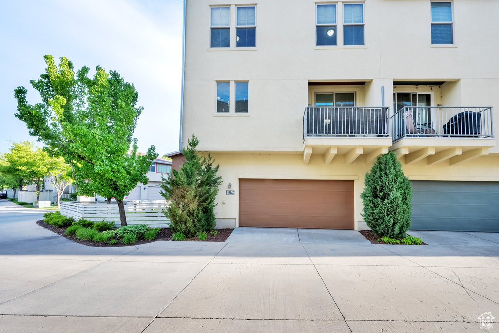 View of front of home featuring stucco siding, driveway, an attached garage, and a balcony