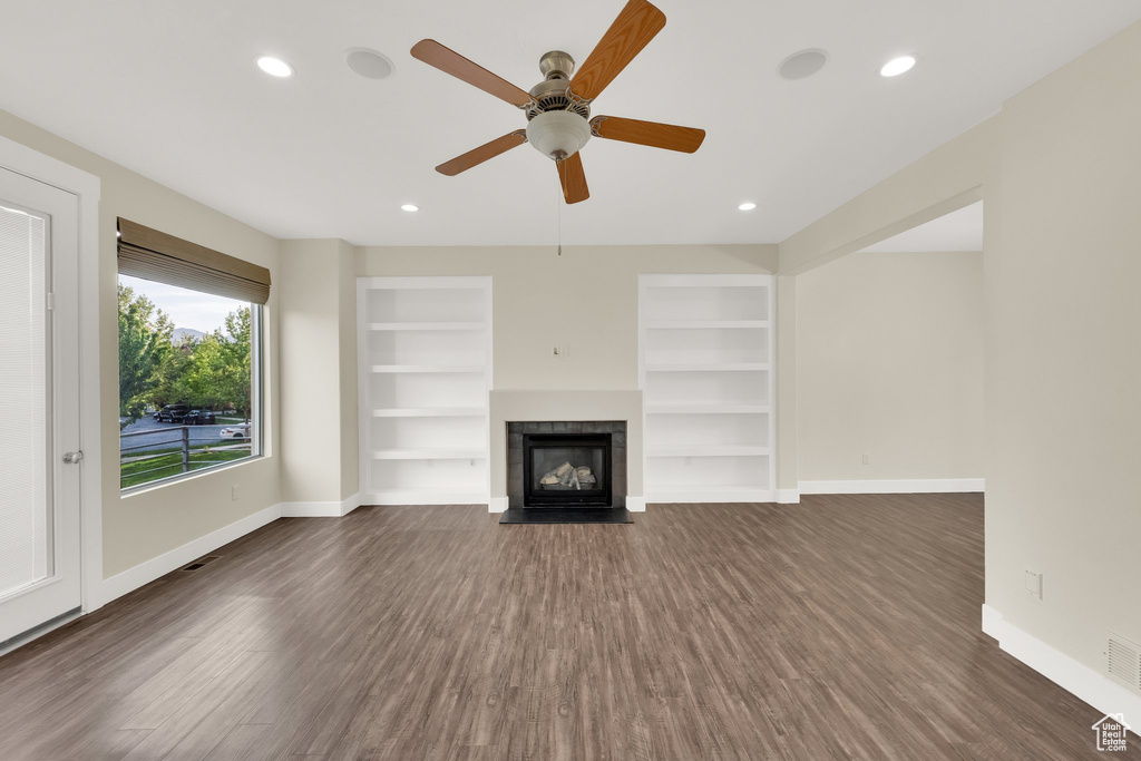 Unfurnished living room featuring baseboards, dark wood-type flooring, a tile fireplace, built in shelves, and recessed lighting