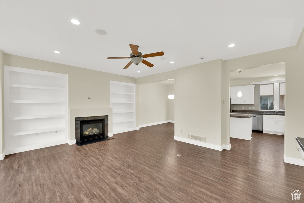 Unfurnished living room featuring dark wood-style floors, baseboards, ceiling fan, built in shelves, and a tiled fireplace