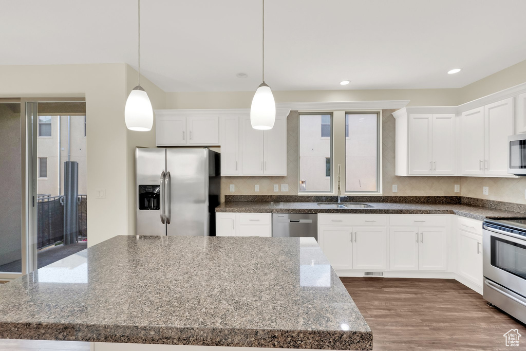 Kitchen featuring appliances with stainless steel finishes, white cabinets, a sink, hanging light fixtures, and recessed lighting