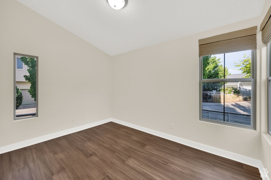 Unfurnished room featuring dark wood-style flooring, baseboards, and lofted ceiling