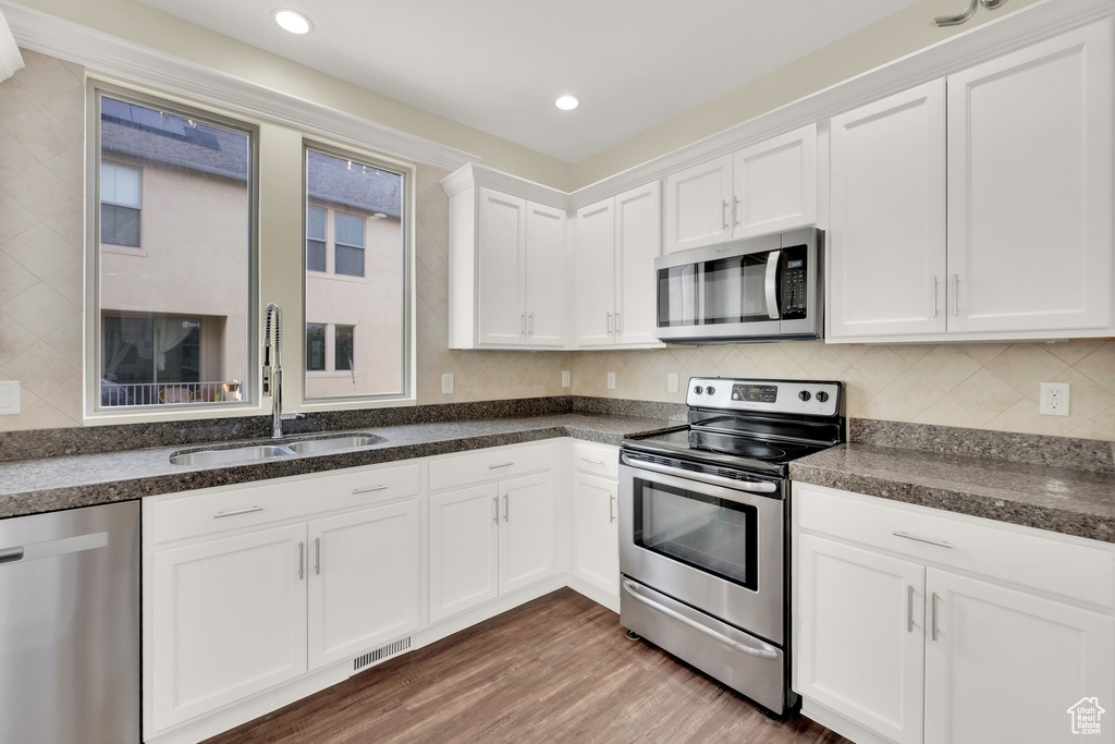 Kitchen featuring stainless steel appliances, a sink, white cabinets, wood finished floors, and recessed lighting