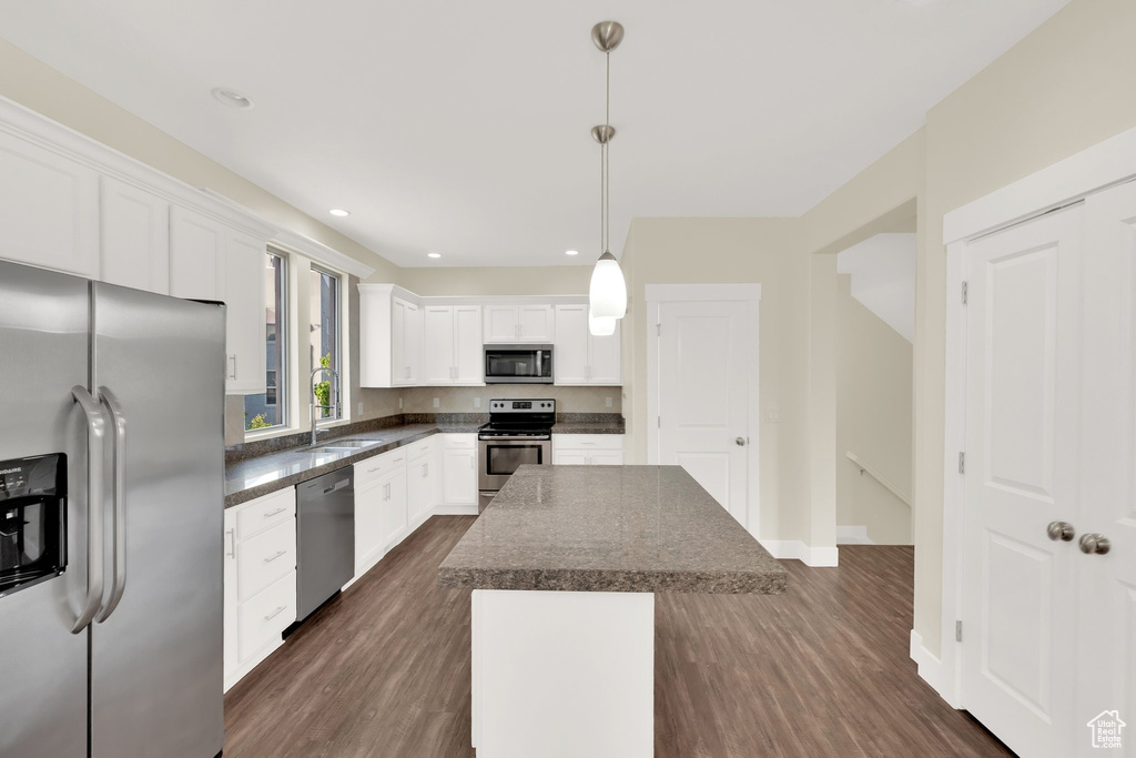 Kitchen with stainless steel appliances, dark countertops, a sink, a center island, and dark wood finished floors