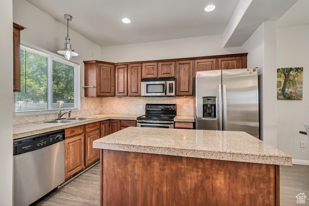 Kitchen with stainless steel appliances, a sink, light wood-style flooring, a center island, and decorative backsplash