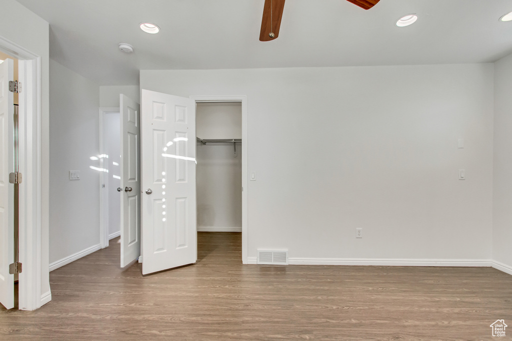 Unfurnished bedroom featuring wood finished floors, baseboards, a walk in closet, a ceiling fan, and recessed lighting