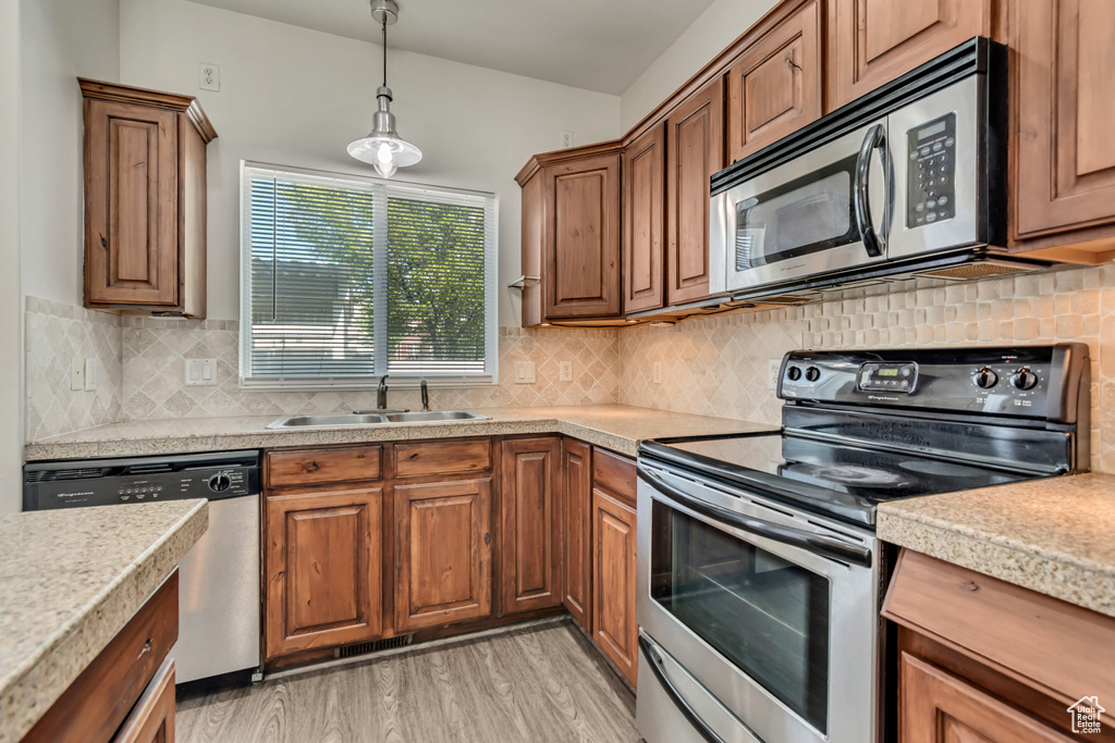 Kitchen with appliances with stainless steel finishes, a sink, light countertops, light wood finished floors, and brown cabinets