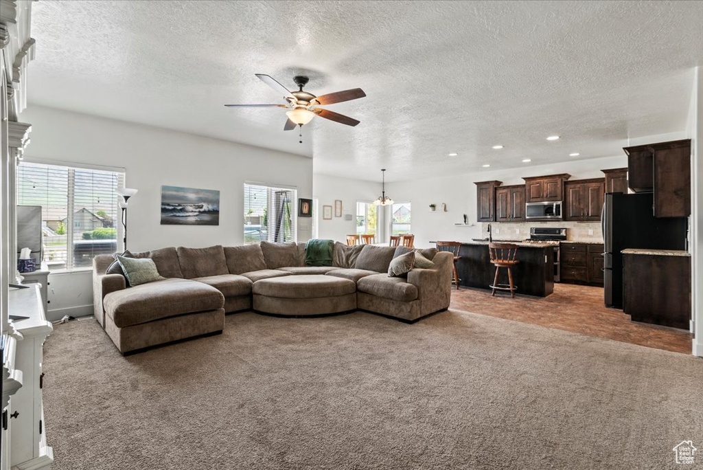 Carpeted living room with healthy amount of natural light, a textured ceiling, ceiling fan, recessed lighting, and a sink