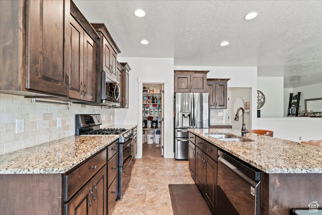 Kitchen with stainless steel appliances, a sink, a textured ceiling, dark brown cabinets, and backsplash