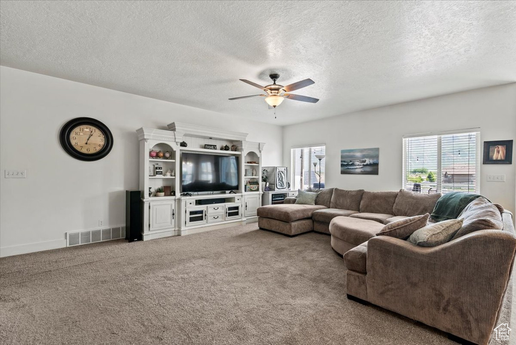 Living area featuring ceiling fan, carpet floors, and a textured ceiling