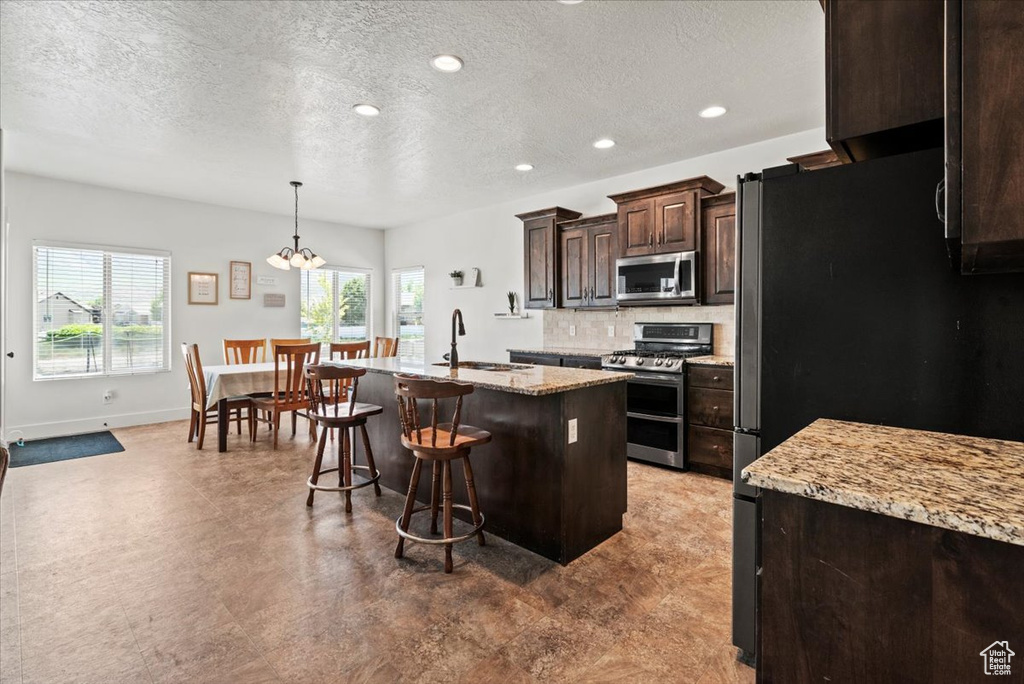 Kitchen with appliances with stainless steel finishes, a sink, a kitchen bar, an island with sink, and dark brown cabinets