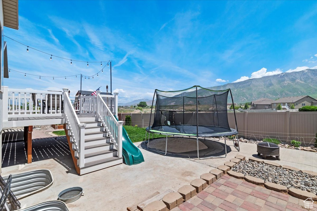 Fenced backyard featuring a trampoline, a fire pit, a patio area, a mountain view, and stairway