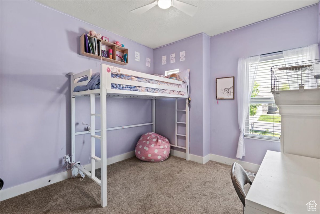 Carpeted bedroom featuring an office area, a ceiling fan, and baseboards