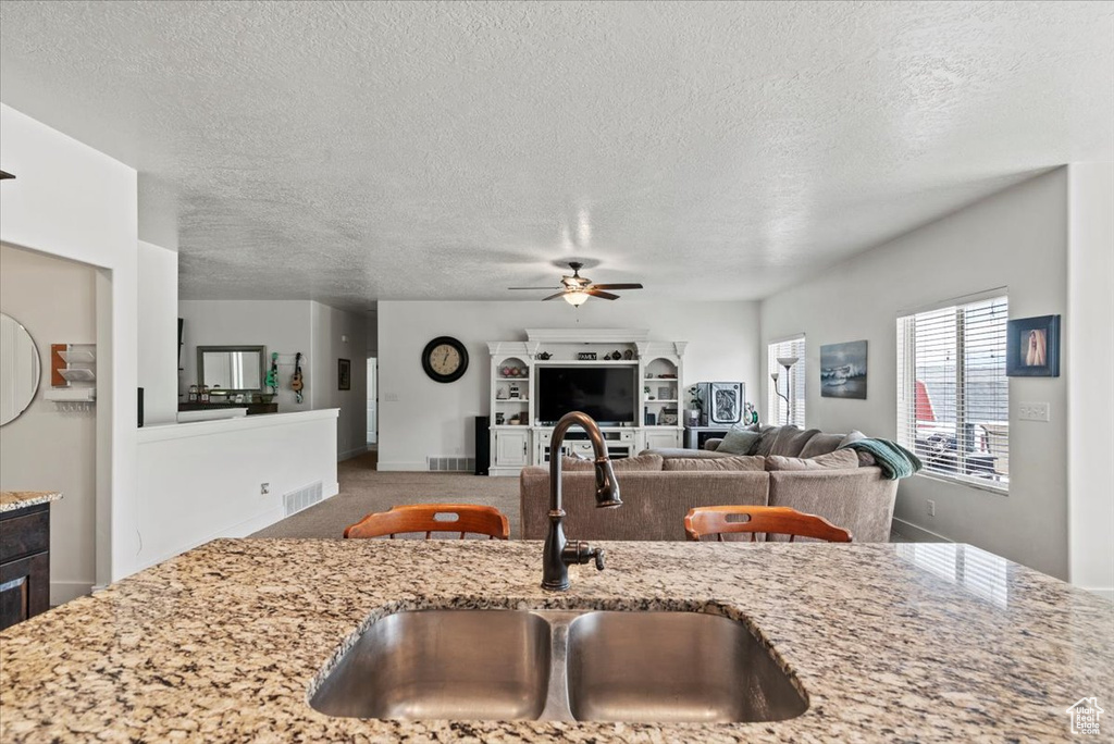 Kitchen with a sink, a ceiling fan, a textured ceiling, light stone countertops, and open floor plan