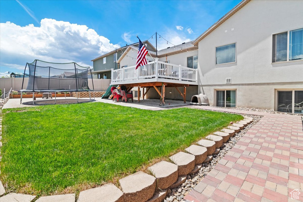 Back of house featuring a trampoline, a wooden deck, stucco siding, and a patio area